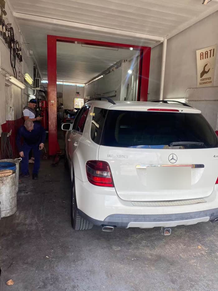 White Mercedes-Benz ML350 parked in the shop bay with technicians working